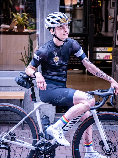 Portret van wielrenner Sebastien Sutherland: heeft tatoeages en een wielrenoutfit aan, zit op een wielrenfiets met een helm op en kijkt naar rechts 